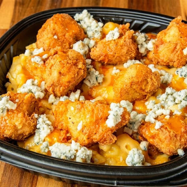 Buffalo chicken mac and cheese with blue cheese crumbles in a black takeout container.