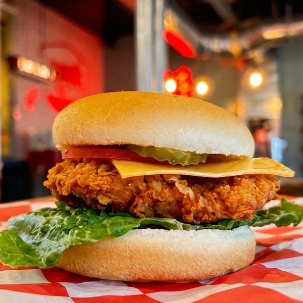 Crispy fried chicken sandwich with lettuce, tomato, cheese, and pickles on a red checkered paper.