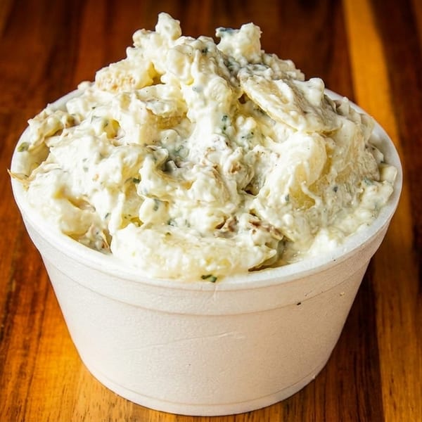 Creamy potato salad with herbs in a white styrofoam cup on a wooden table.