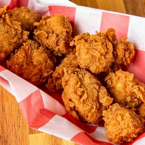 Crispy fried chicken pieces in a red and white checkered paper tray on a wooden table.