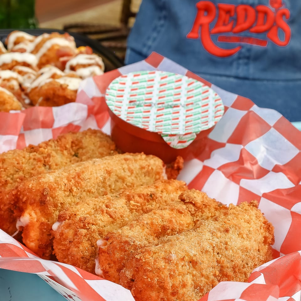 Crispy breaded fried food served in red-and-white checkered baskets, with sauced wings and dipping sauce visible behind.